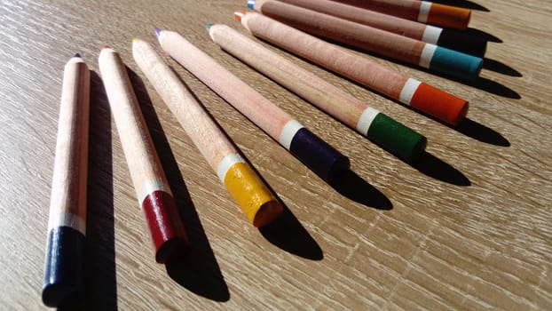 On a wooden table are wooden thick colored pencils.