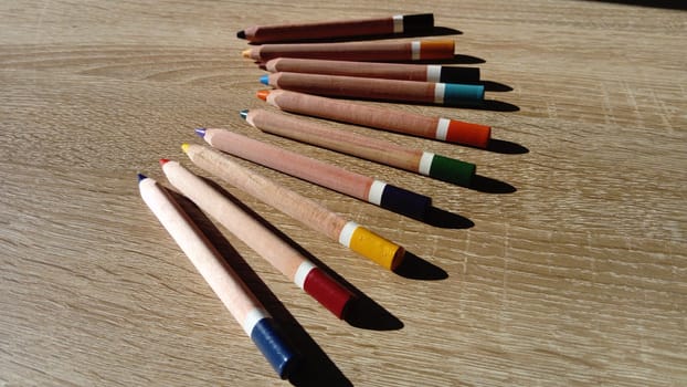 On a wooden table are several wooden thick colored pencils.