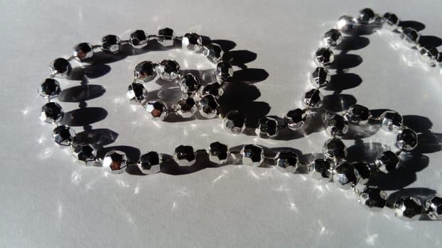 A shiny bracelet on a hand lies on a white surface. Beads sparkle in the light