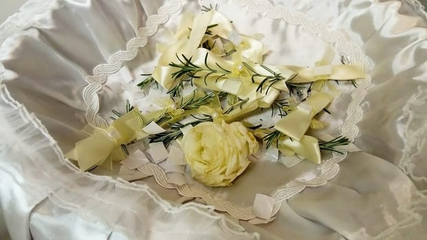 A few twigs of rosemary pinned to the festive wedding bows. The jewelry lies with a white rose in a basket on a silk decorative pillow. Used as a decoration for guests at a wedding.