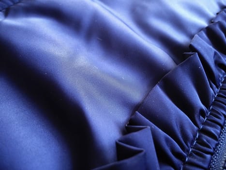 A fragment of a garment made of synthetic polyester fabric. The play of light and shadow on blue material. Right - sewn decorative element in the form of a shuttlecock.