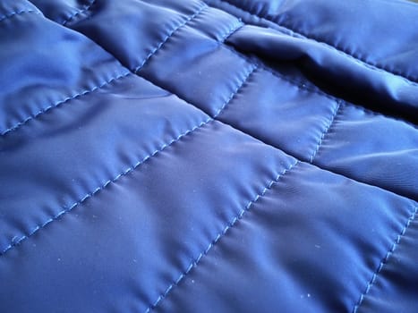 Quilted sports jacket fabric sample. Blue polyester material soaked in rain and wind. Smooth, high-quality, accurate seams.