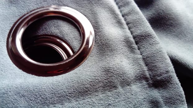 close-up of a metal eyelet on a gray-blue curtain made of thick velvety fabric.