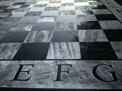 Stone table with a chessboard. Black and white chess fields. The letters E, F and G. Reflection of light on a polished surface. Monochrome squares.