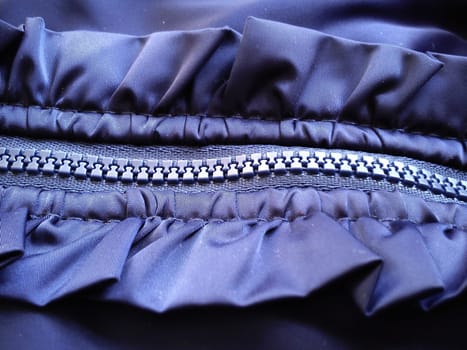 Buttoned sewing lock on a piece of blue polyester fabric. There are decorative flounces on the sides of the neat seams. Sewing lock horizontal position.