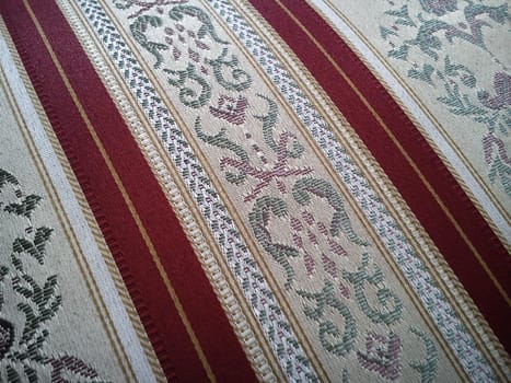 A sample of dense fabric for upholstery of upholstered furniture. The pattern of floral and floral elements in beige shades is combined with wide dark red stripes