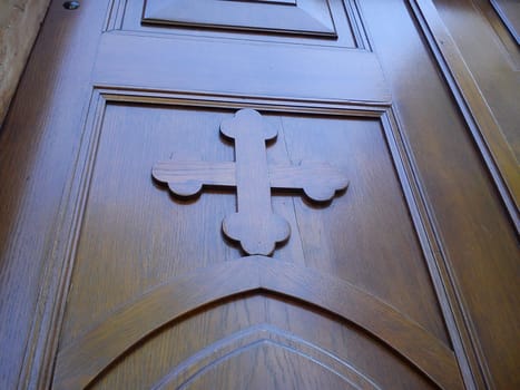 Wooden old church door. Carved wooden cross and varnished, smooth surface, shining in natural light.