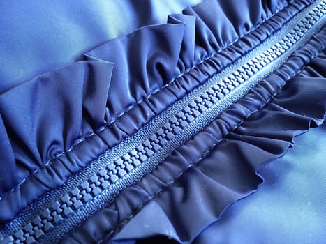 Buttoned sewing lock on a women's blue synthetic fabric jacket. On the sides of the even seams there are decorative elements in the form of shuttlecocks.