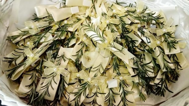 A few twigs of rosemary pinned to the festive wedding bows. The jewelry lies in a basket on a silk decorative pillow. Used as a decoration for guests at a wedding.