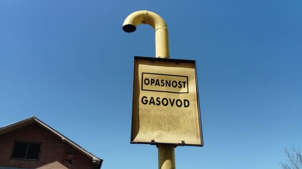 Gas sign with inscriptions in Serbian, Montenegrin and Croatian - be careful Gas. Metal crumpled sign on a blue sky background. Gas pipeline laying through the countryside. Serbia, Sremska Mitrovica.