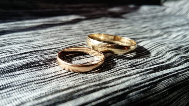 two gold wedding rings on a polo background with reflections of the sun's rays on the background