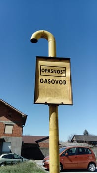 Gas sign with inscriptions in Serbian, Montenegrin and Croatian - be careful, gas. Metal warning sign against the blue sky and buildings. Gas pipeline laying. Serbia, Sremska Mitrovica.