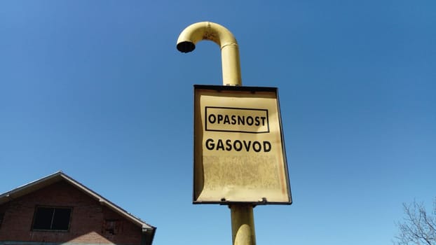 Gas sign with inscriptions in Serbian, Montenegrin and Croatian - be careful Gas. Metal crumpled sign on a blue sky background. Gas pipeline laying through the countryside. Serbia, Sremska Mitrovica.