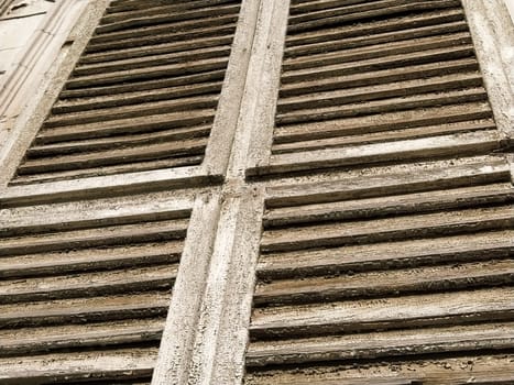Old wooden shutters on the window. Antique wooden architecture. Dry wood with rustling discolored paint. Husk and dust. Natural color. Window sill, horizontal stripes and slats.