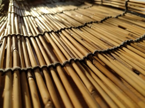 A straw bedding, tablecloth or small rug laid on a table and photographed from the side. Soft evening sunlight reflects off the stems. Some sticks are broken, threads and ropes are braided.