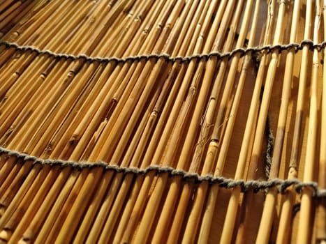 A straw bedding, tablecloth or small rug laid on a table and photographed from the side. Soft evening sunlight reflects off the stems. Some sticks are broken, threads and ropes are braided.
