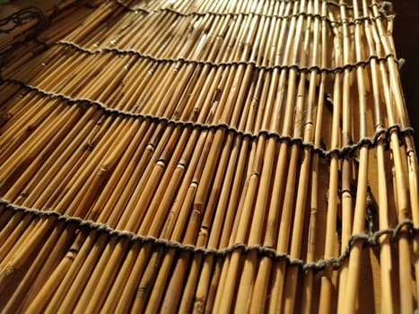 A straw bedding, tablecloth or small rug laid on a table and photographed from the side. Soft evening sunlight reflects off the stems. Some sticks are broken, threads and ropes are braided.