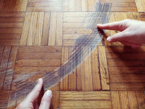 Old, scratched parquet flooring needs maintenance. the parquet is damaged by scratches from prolonged use. Master's hands show damage to the floor