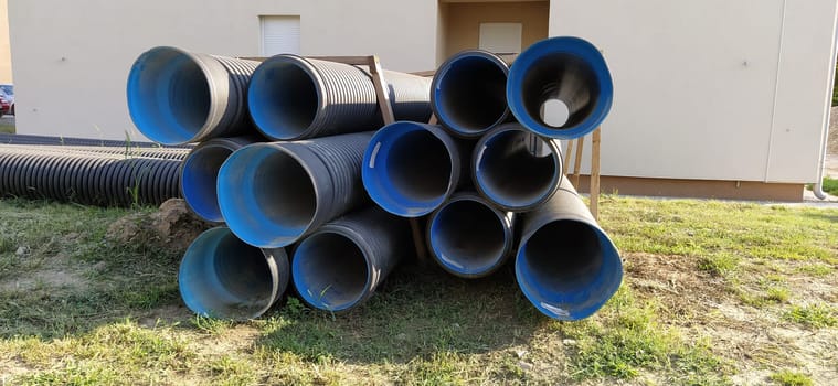 Sremska Mitrovica, Serbia, 23 August 2020. Metal corrugated pipes, blue inside. Plumbing or heating pipes lie on the ground next to a residential building. Corrugated metal. Production of technical and construction pipes