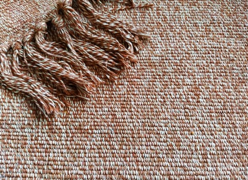Woven fabric with tassels. Coarse weaving cotton. Floor mat. Beige, white and wrinkled threads in weaving. Woolen or acrylic material.