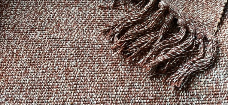 Woven fabric with tassels. Coarse weaving cotton. Floor mat. Beige, white and wrinkled threads in weaving. Woolen or acrylic material