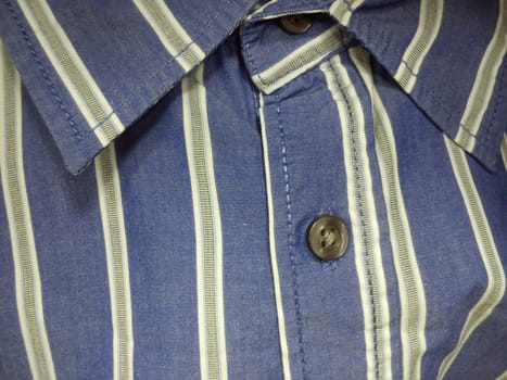 Collar and button on a mans shirt. Gva blue thread, brown button. Striped gray-blue fabric on casual wear. Assortment of men's wardrobe in the store. Close-up.