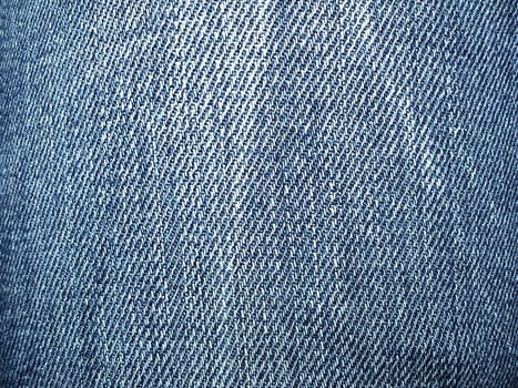 Blue denim. Texture of cotton coarse material. A fragment of a natural rag indigo. Vertical furrows, dark and light threads, individual stitches are noticeable. Crumpled spots on a piece of fabric.
