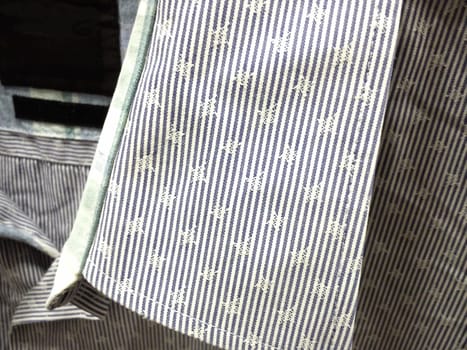 Collar on a mans shirt. White blue striped fabric on casual wear. Assortment of men's wardrobe in the store. Close-up.