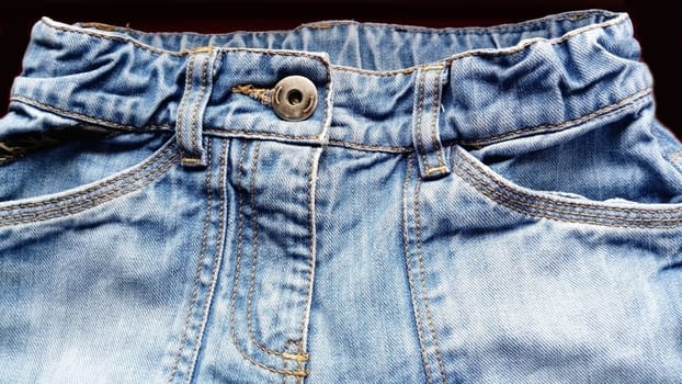 Blue denim jeans. Texture of cotton coarse material. A fragment of a natural rag indigo. Vertical furrows, dark and light threads, individual stitches are noticeable