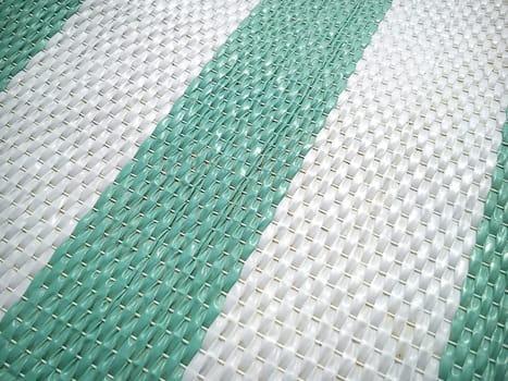 Green and white synthetic burlap, close-up. Polyethylene material. Interlacing of polyethylene fibers and threads. Striped beach mat or sports mat.