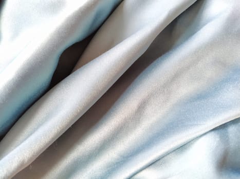 Silky to the touch fabric of gray - blue color with a brilliant shimmer. Natural lighting, light and shadow. The material is casually folded. Polyester Textile.
