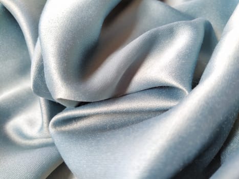Silky to the touch fabric of gray - blue color with a brilliant shimmer. Natural lighting, light and shadow. The material is casually folded. Polyester Textile.