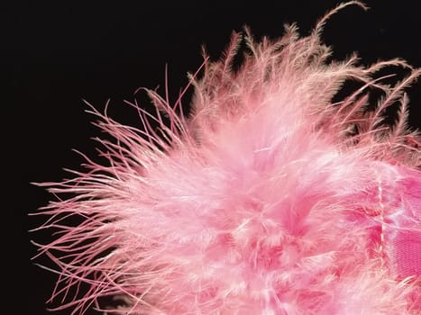 Delicate pink fluff on a black background. Real fur with a long pile. Close-up. Boa or cosmetic brush. Graceful details. Soft focus. Blurred image.