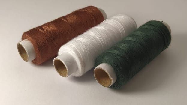 Bobbins and spools of thread of different colors - brown, white and green. Close-up. Natural light on the left side. Skeins of thread. Sewing supplies.