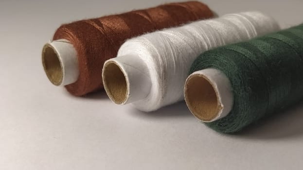 Bobbins and spools of thread of different colors - brown, white and green. Close-up. Natural light on the left side. Skeins of thread. Sewing supplies. Textile production