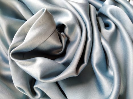 Silky to the touch fabric of gray - blue color with a brilliant shimmer. Natural lighting, light and shadow. The material is casually folded. Polyester Textile