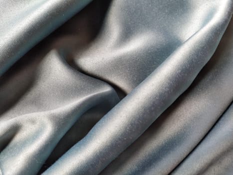Silky to the touch fabric of gray - blue color with a brilliant shimmer. Natural lighting, light and shadow. The material is casually folded. Polyester Textile