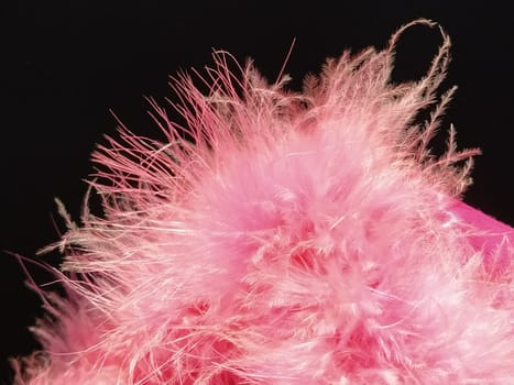 Delicate pink fluff on a black background. Real fur with a long pile. Close-up. Boa or cosmetic brush. Graceful details. Soft focus. Blurred image.