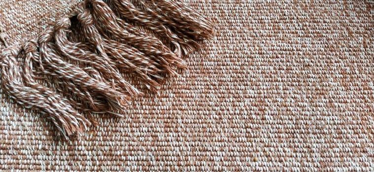 Woven fabric with tassels. Coarse weaving cotton. Floor mat. Beige, white and wrinkled threads in weaving. Woolen or acrylic material.