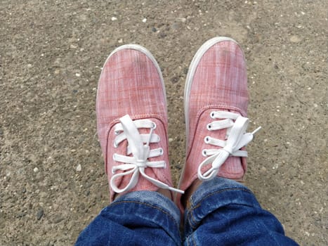 Pink sneakers with white laces on the legs. Blue jeans wrapped underneath. View from above. Carefree and sporty