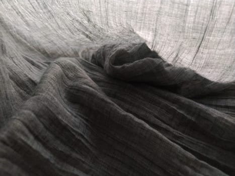 Light translucent curtains or tulle in the Scandinavian style. Gray pleated fabric or wrinkled textile hangs down. Close-up. The bottom edge of the curtain lies on a horizontal surface. Soft focus.