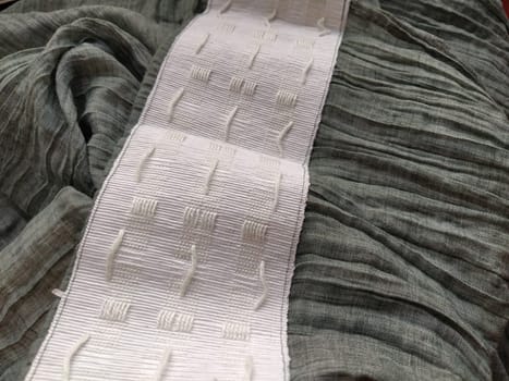 wide white curtain tape sewn to gray pleated fabric. Finishing the top of a curtain or light tulle