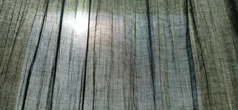 the sun is visible through the gray pleated curtains. Scandinavian style. Pastel colors on the fabric. The curtain is translucent, through which you can see what is happening on the street.