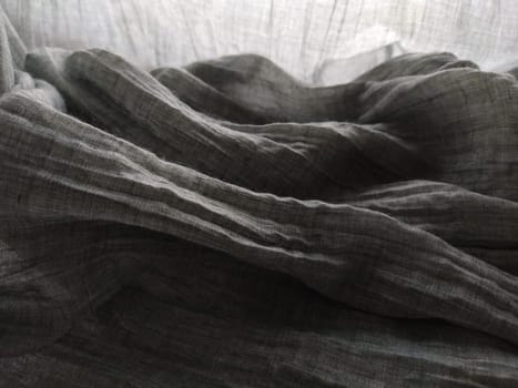 Light translucent curtains or tulle in the Scandinavian style. Gray pleated fabric or wrinkled textile hangs down. Close-up. The bottom edge of the curtain lies on a horizontal surface. Soft focus