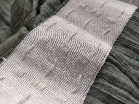 wide white curtain tape sewn to gray pleated fabric. Finishing the top of a curtain or light tulle.