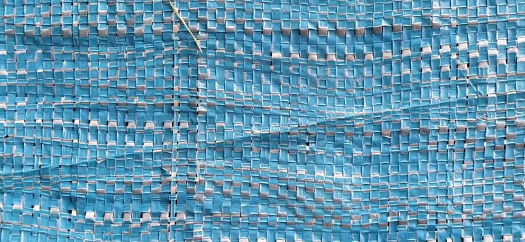 Blue synthetic burlap, close-up. Polyethylene material. Interlacing of polyethylene fibers and threads. Folds and bruises. Packing and packaging material.