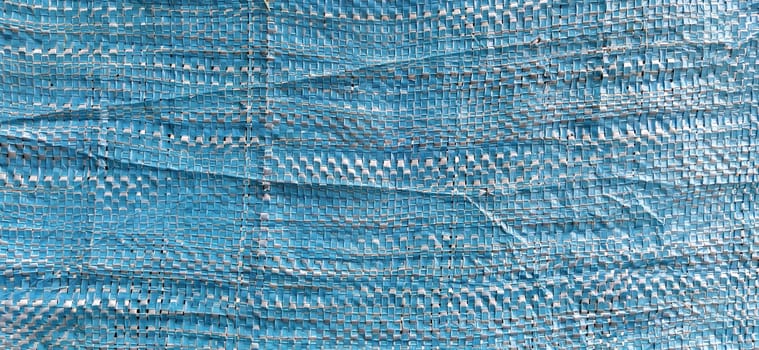 Blue synthetic burlap, close-up. Polyethylene material. Interlacing of polyethylene fibers and threads. Folds and bruises. Packing and packaging material.