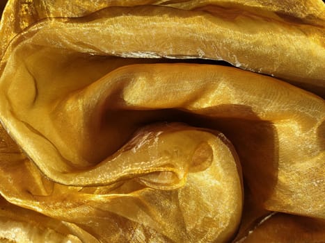 Organza is yellow-brown with a beige sheen. Shiny, reflective, beautiful fabric for curtains, tulles. Interior design option. Twisted, casually folded organza section in sunlight.