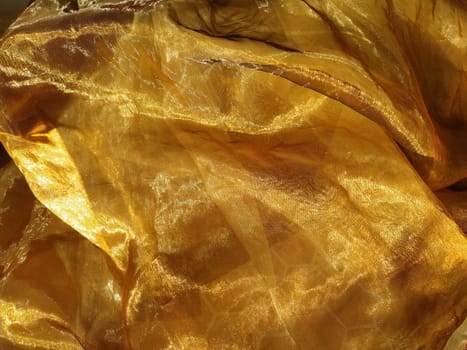 Organza is yellow-brown with a beige sheen. Shiny, reflective, beautiful fabric for curtains, tulles. Interior design option. Twisted, casually folded organza section in sunlight.
