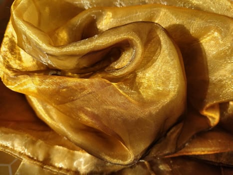 Organza is yellow-brown with a beige sheen. Shiny, reflective, beautiful fabric for curtains, tulles. Interior design option. Twisted, casually folded organza section in sunlight.